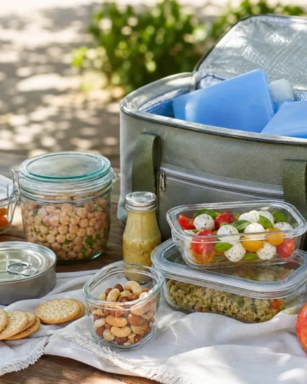 Pique-nique avec glacière, bocaux en verre, fruits et conserves sur une table en extérieur